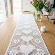 White filet crochet table runner with heart and flower grid pattern on an oak dining table